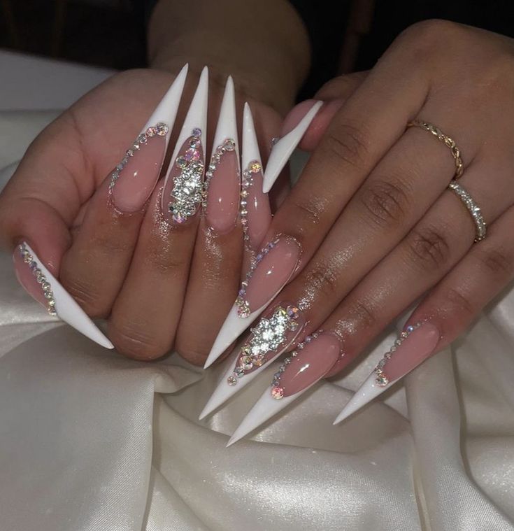 Elegant Stiletto Nails: Nude and White Design Accentuated with Rhinestones and Intricate Embellishments