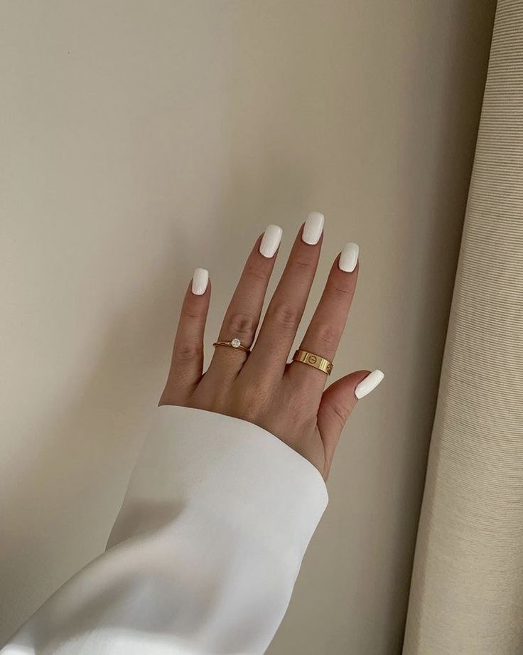 Elegant White Almond-Shaped Manicure Accented with Delicate Gold Rings for a Chic Look.