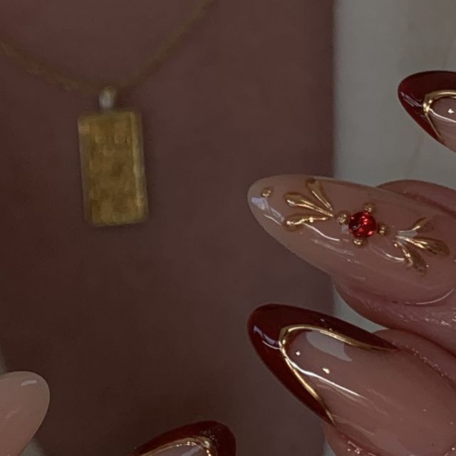 Elegant Almond-Shaped Nails: Glossy Burgundy Tips with Golden Floral Designs and Red Gem Embellishments.