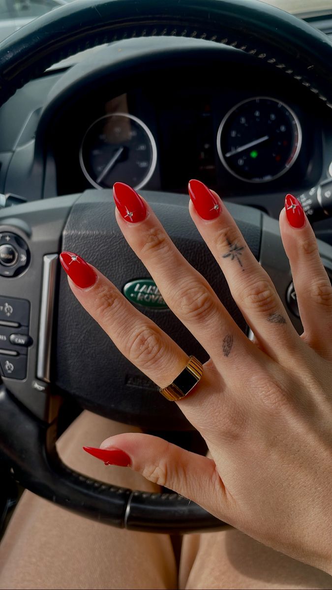 Bold Red Stiletto Nails with Whimsical Silver Accents and Chic Gold Ring for a Statement Look.