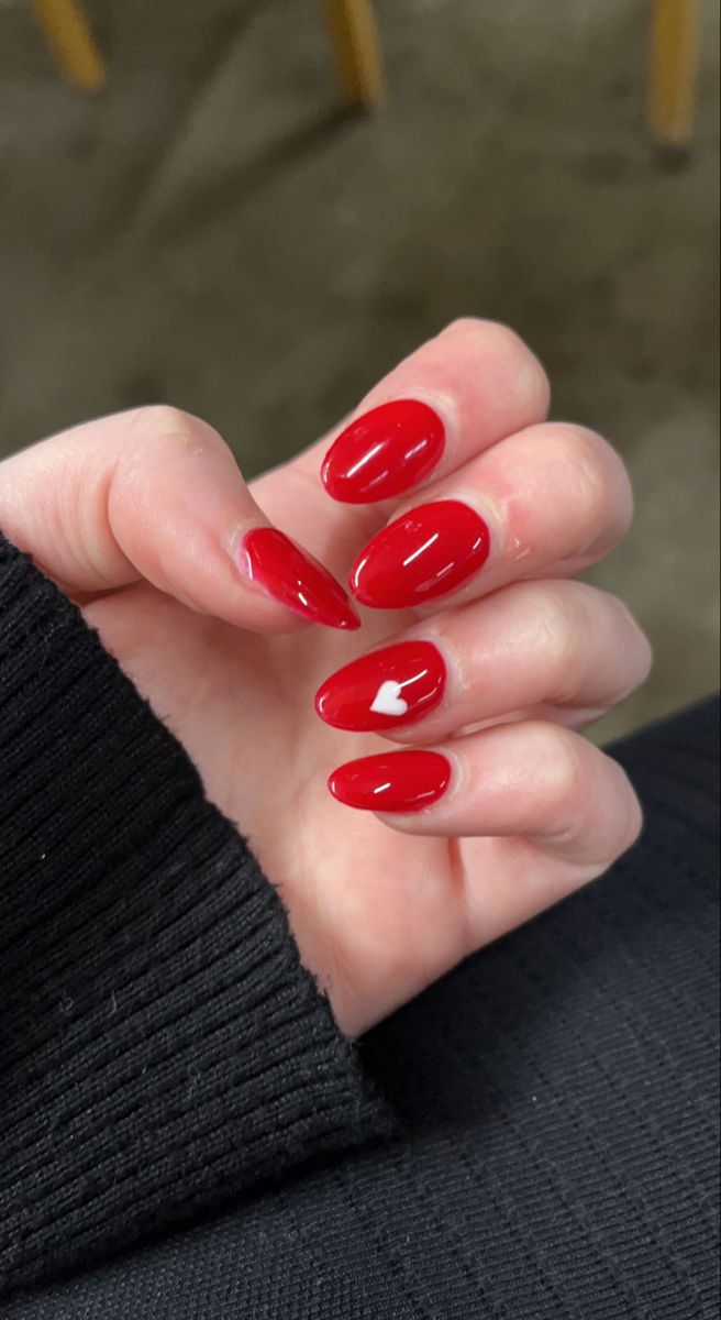 Eye-Catching Glossy Red Almond Nails with Playful Heart Accent.