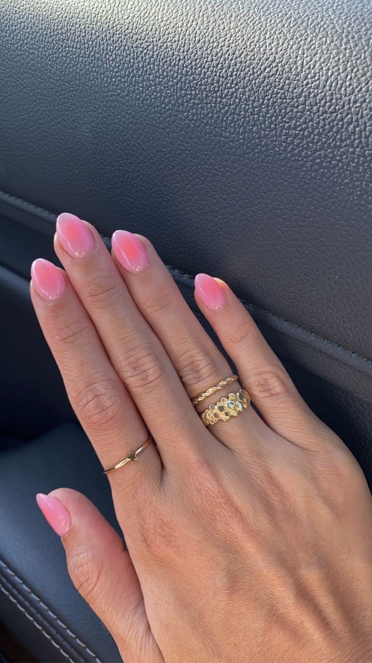 Elegant Oval Pink Manicure with Shiny Finish and Chic Gold Rings.