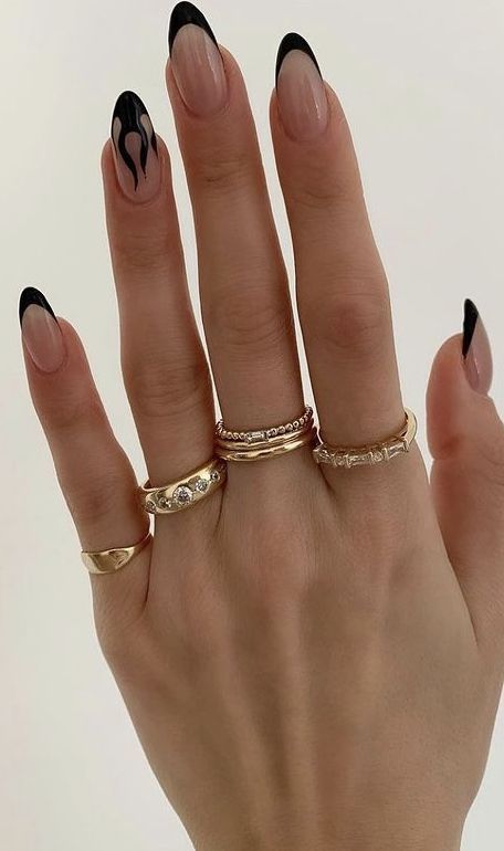 Chic Nude Nail Design with Striking Black Tips and Artistic Flame Patterns, Accented by Delicate Gold Rings.