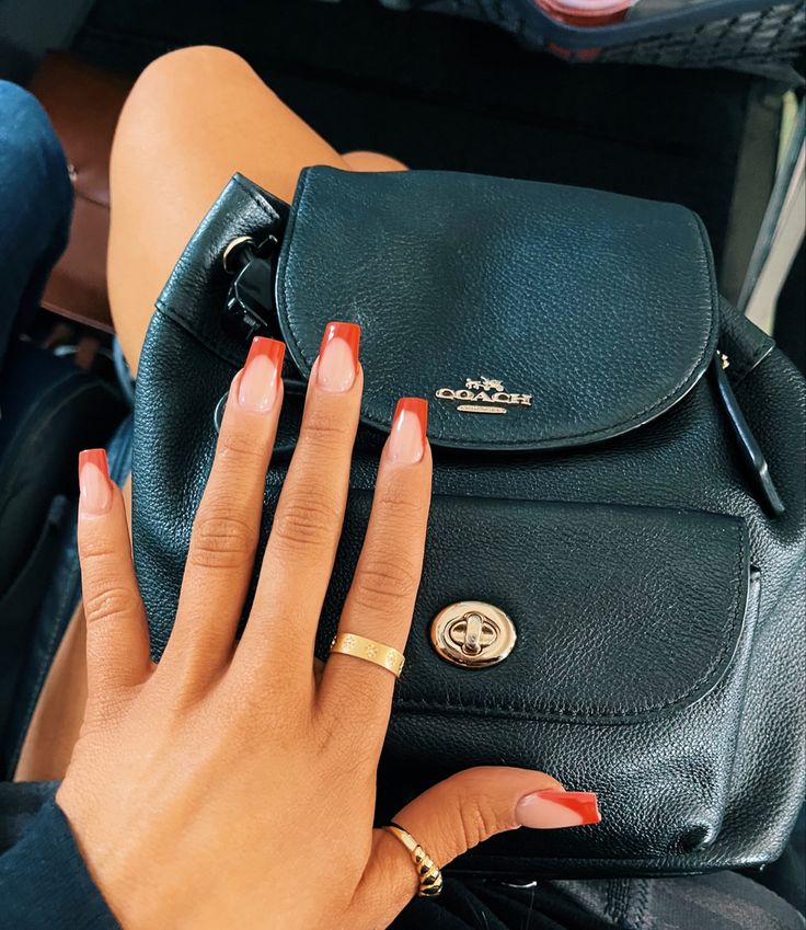 Chic Ombre Nail Design: Soft Peach to Vibrant Red Tips Complementing a Black Handbag.