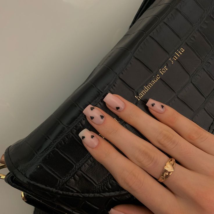 Chic Nude Nail Design with Heart Accents, Complemented by a Stylish Black Handbag and Luxurious Gold Ring.