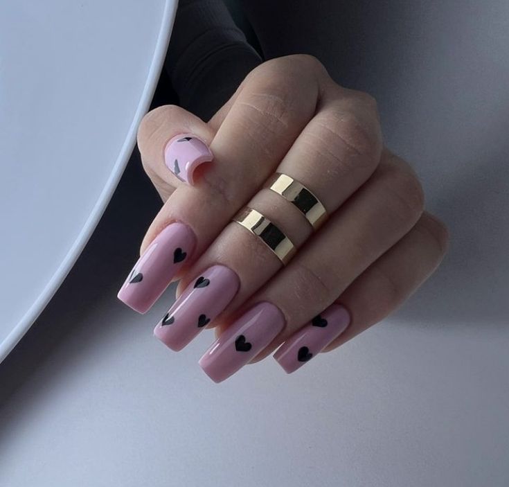 Elegantly Playful Chic Nail Design: Soft Pink Base with Black Heart Accents and Gold Ring Compliments.