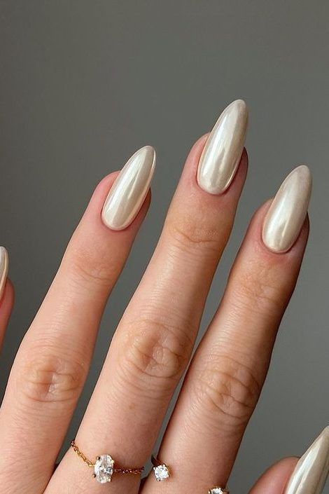 Sophisticated Almond-Shaped Nails in Shimmering Beige with Glossy Finish and Delicate Gold Accents.