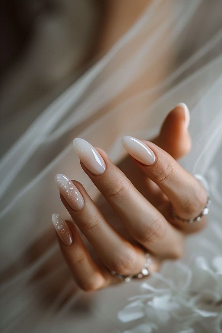 Sophisticated Almond-Shaped Nails in Soft White with Glamorous Accents for Elegant Occasions.