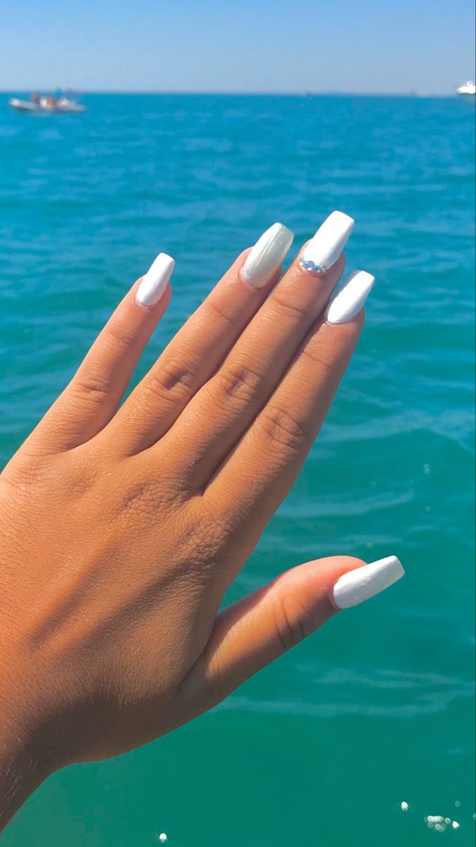 Chic White Manicure with Gemstone Accent Set Against Serene Ocean Backdrop.