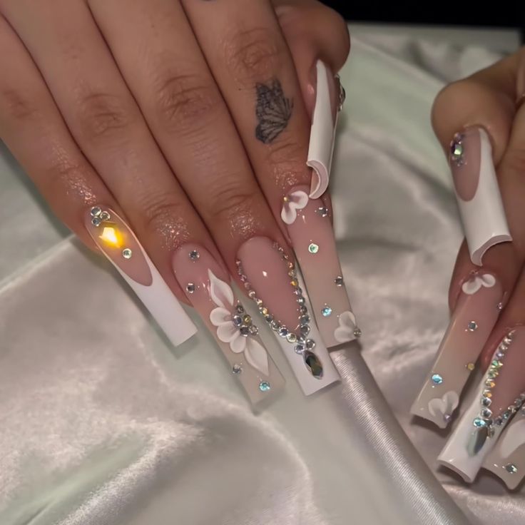 Elegant Long Square Nail Design with Nude Polish, White Tips, Floral Patterns, and Sparkling Rhinestones.