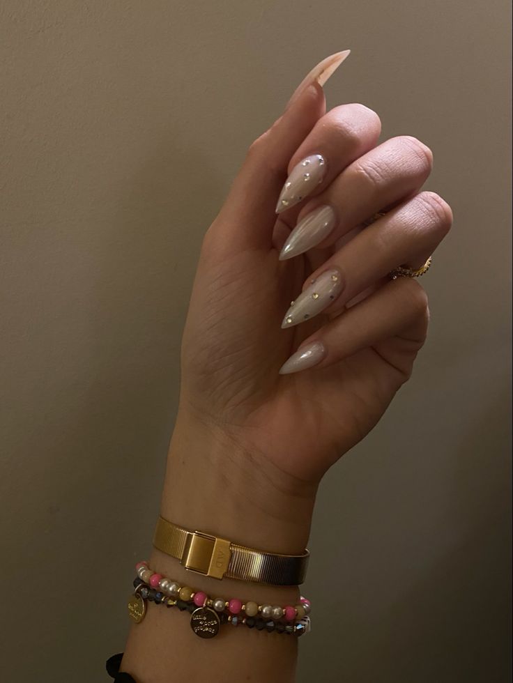 Chic Almond-Shaped Nude Nails Adorned with Shimmering Gems and Stylish Bracelets for Effortless Elegance.