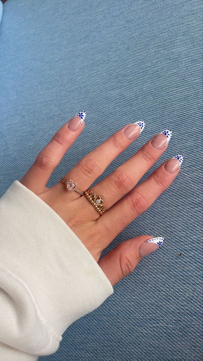 Playful Nude Nail Design with Blue and White Polka Dot Tips, Enhanced by Delicate Rings.