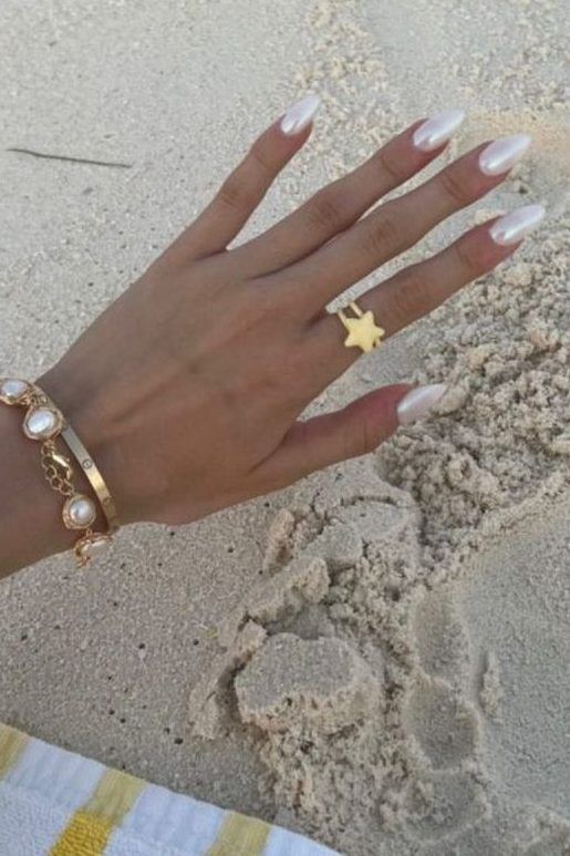 Luxurious Almond-Shaped Nails in Soft White with Gold Jewelry Against a Beachy Backdrop