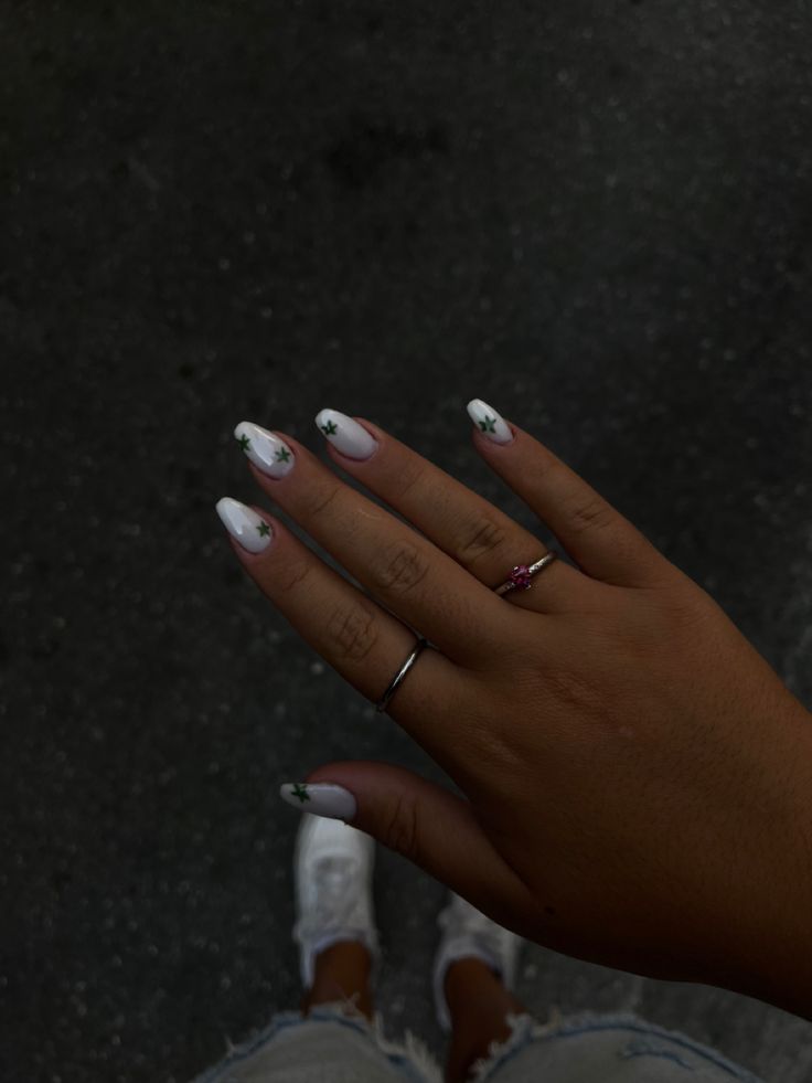 Elegantly Chic: White Nails with Green Star Accents and Minimalist Rings.