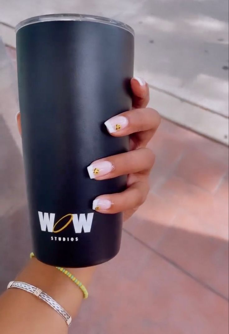 Chic French Tip Nail Design with Floral Accents and Sleek Black Tumbler