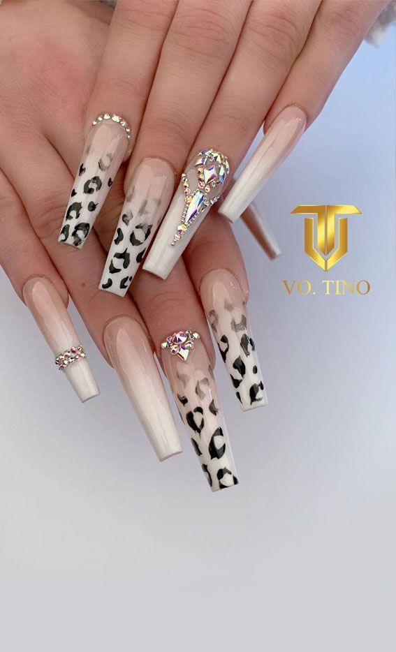 Chic Elongated Nail Design with Nude and White Tones, Leopard Print Tips, and Sparkling Rhinestone Accents.