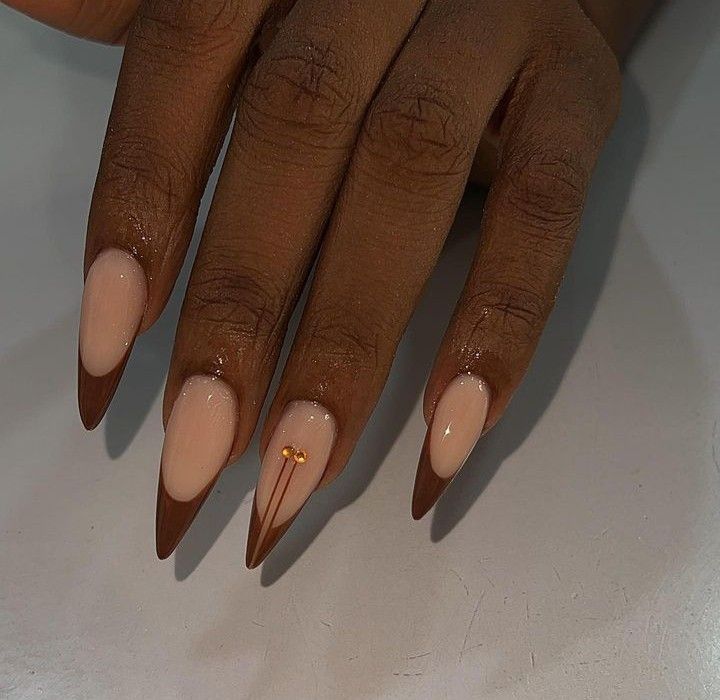 Chic Almond-Shaped Nails: Soft Nude Base with Striking Brown Tips and Gold Accents.