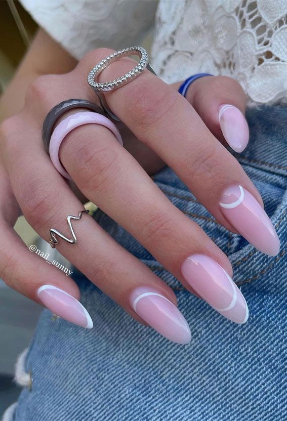 Chic Almond-Shaped Nails with Soft Pink Base and White Crescent Tips, Enhanced by Minimalistic Rings.