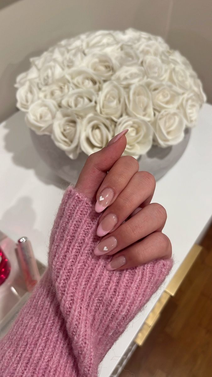 Chic Nail Design: Soft Nude Base with Glossy Accents and Playful Heart Details, Paired with a Cozy Pink Sweater.