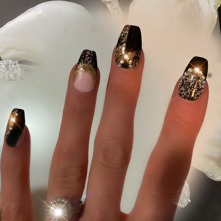 Sophisticated Nail Design: Glossy Black and Sparkling Gold Accents with Glamorous Embellishments.