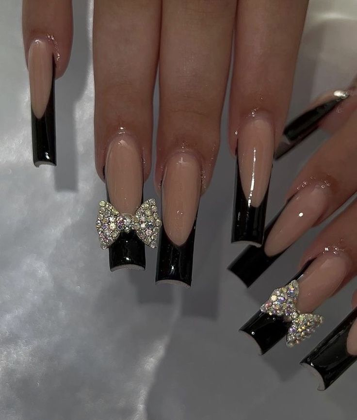 Chic Nail Design: Nude and Glossy Black Polish with Rhinestone Bow Accents.