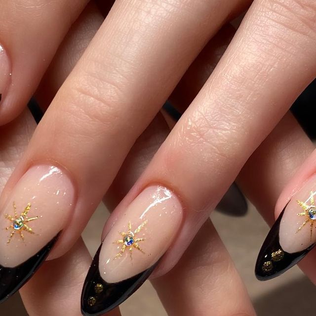 Chic Nude Nail Design with Gold Starbursts, Black Tips, and Sparkling Rhinestones