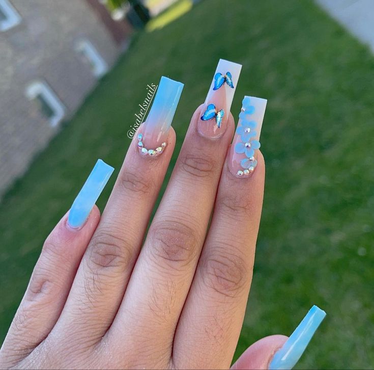 Vibrant Blue Ombre Nails with Rhinestones and Floral Accents for a Chic Summer Look.