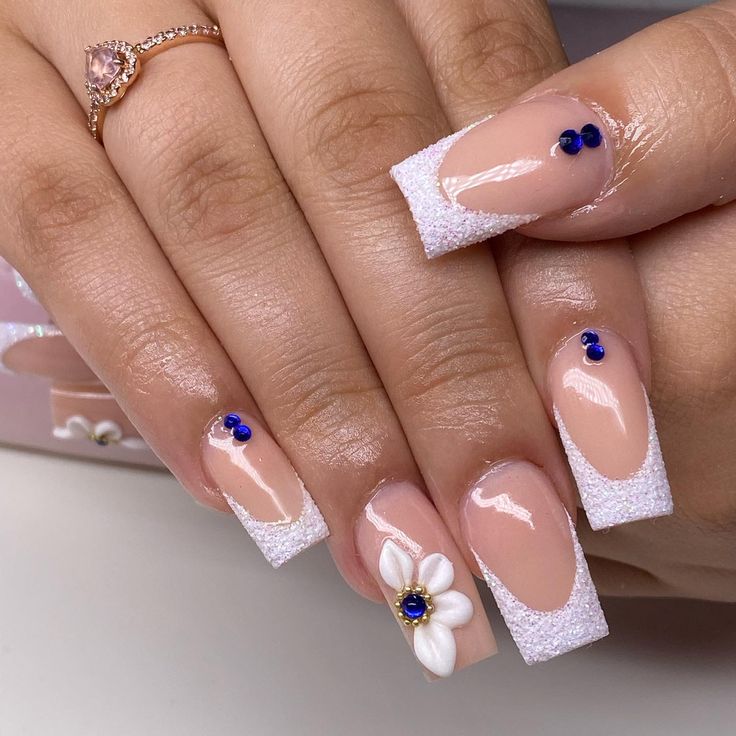 Chic French Tip Manicure with Sparkling Glitter, Floral Accents, and Gemstone Elegance.