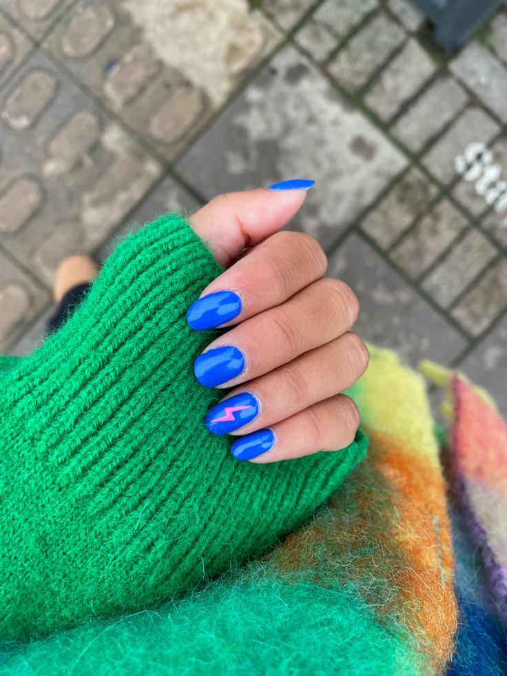 Striking Blue Nail Design with Playful Lightning Bolt Accents and Contrasting Green Sweater.