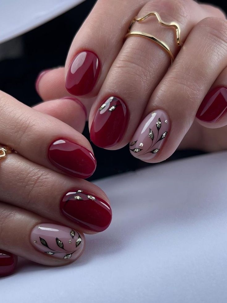 Sophisticated Burgundy and Nude Nail Design with Delicate Leaf Patterns and Gold Accents.