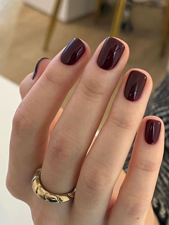 Sophisticated Deep Burgundy Manicure Enhanced by Glossy Finish and Chic Gold Ring.