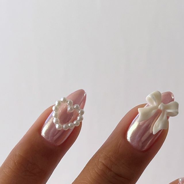 Romantic and Sophisticated Soft Pink Nail Design with Pearl Hearts and Bow Embellishments.