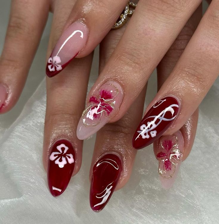 Elegant Floral Nail Design with Deep Red, Soft Pink, Hand-Painted White Flowers, and Gold Accents in Almond and Stiletto Shapes.