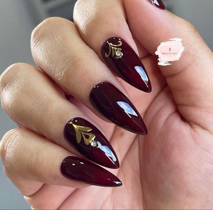 Sophisticated Burgundy Almond Nails with Golden Floral Designs and Subtle Sparkle.