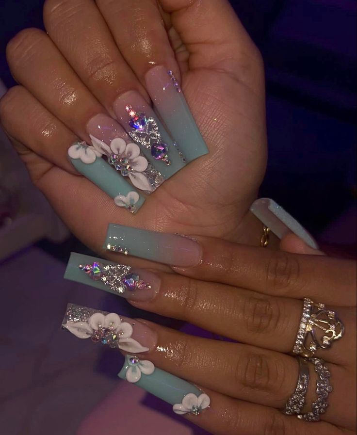 Stunning Pastel Blue Nails Adorned with Delicate Flowers and Rhinestones for an Elegant Look.