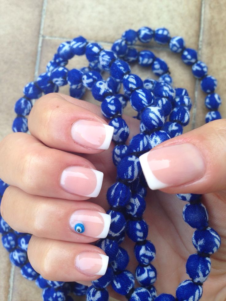 Elegant French Manicure with Eye Accent Nail and Vibrant Blue Beads.