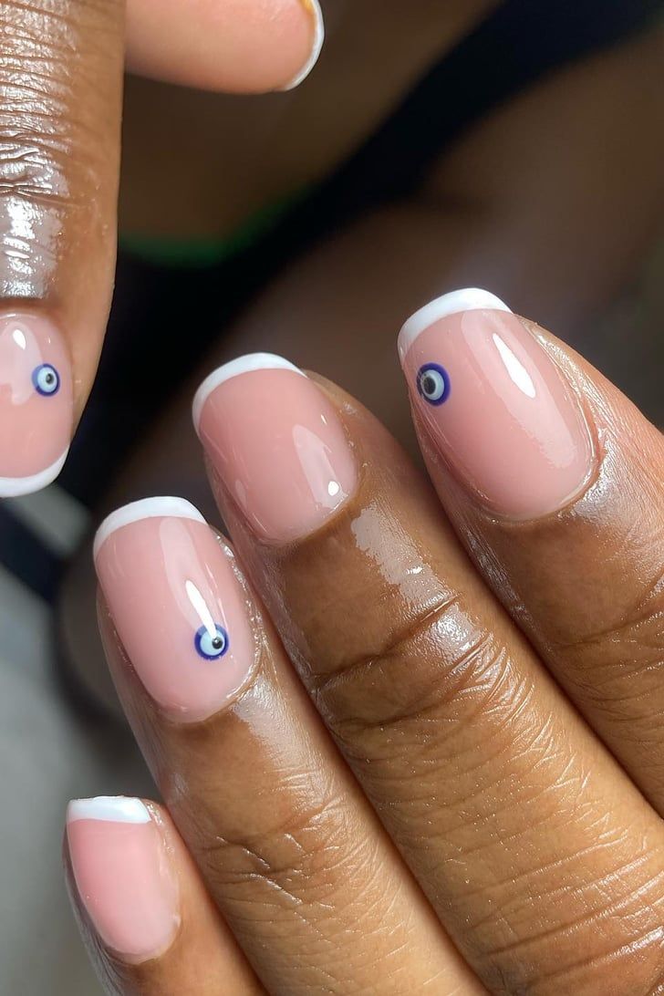 Chic Elegant Nail Design: Soft Nude Base with Classic French Tips and Intricate Blue Evil Eye Accents.