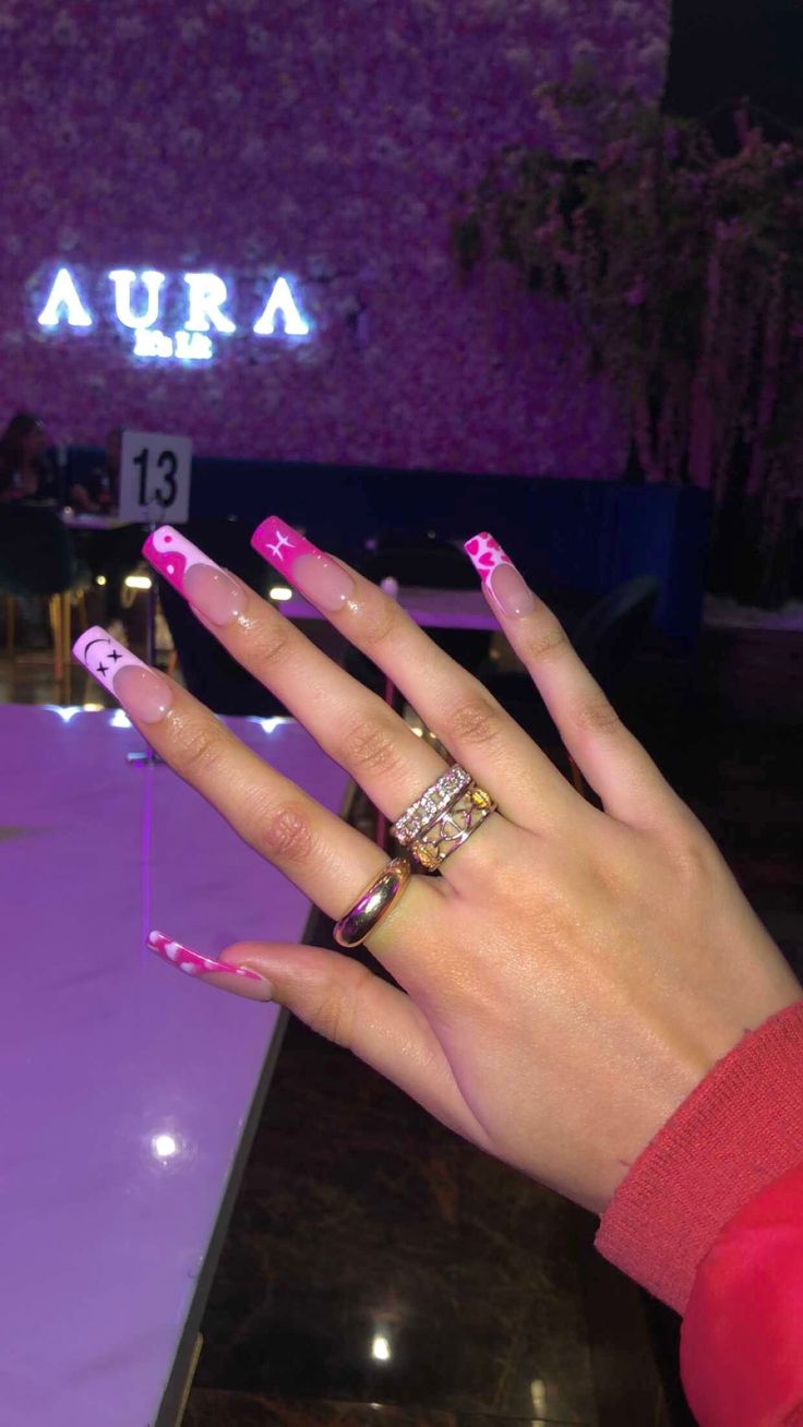 Vibrant Pink and White Long Nails with Playful Star and Heart Designs, Enhanced by Elegant Rings.