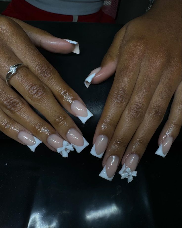 Charming French Tip Manicure: Soft Nude Base with Glossy White Tips and Playful Bow Accents.