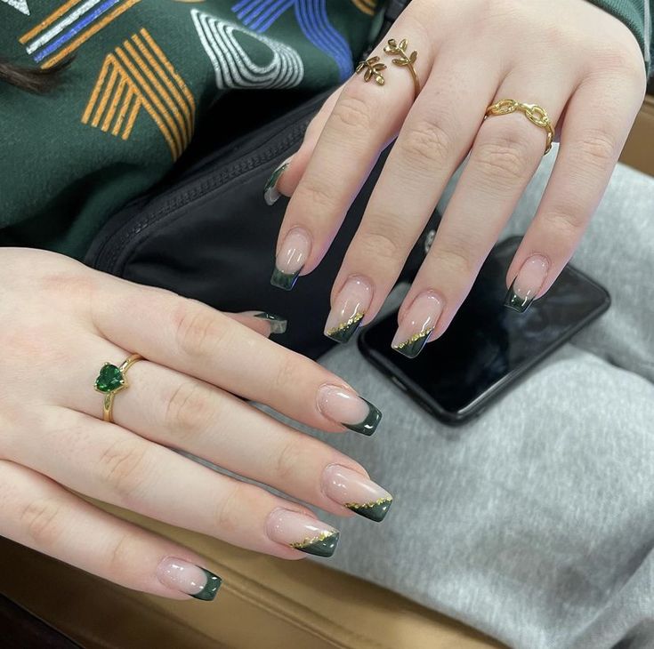 Chic French Tip Nail Design: Nude and Dark Green with Gold Accents and Complementary Rings.