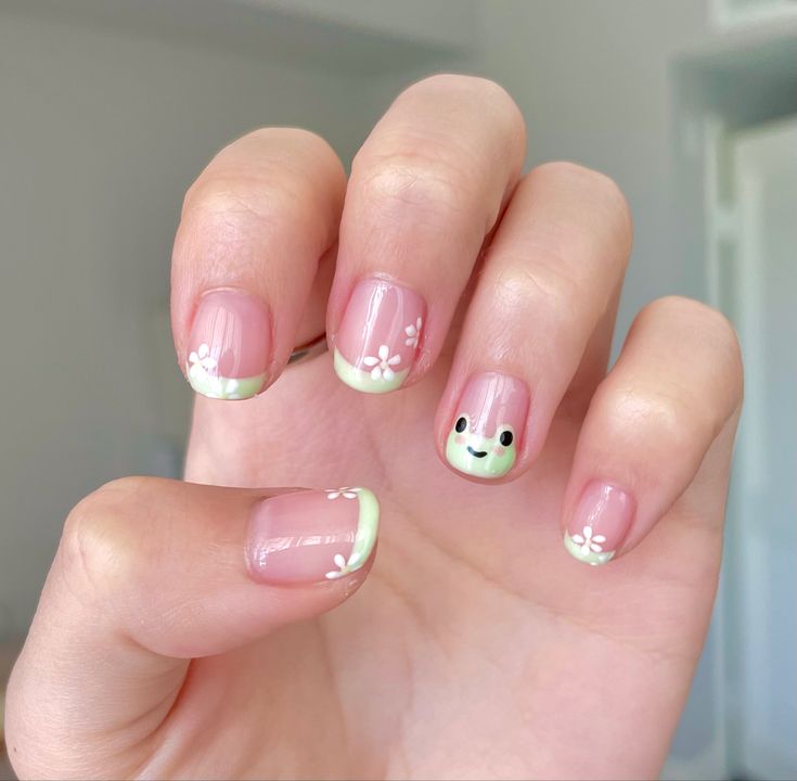 Charming Playful Nail Design with Soft Pink Base, White Flowers, and Whimsical Frog Accent.