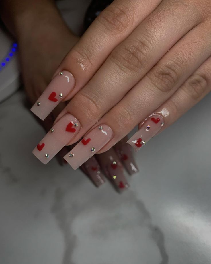 Playful and Chic Nude Nail Design with Vibrant Red Hearts and Glamorous Rhinestones.