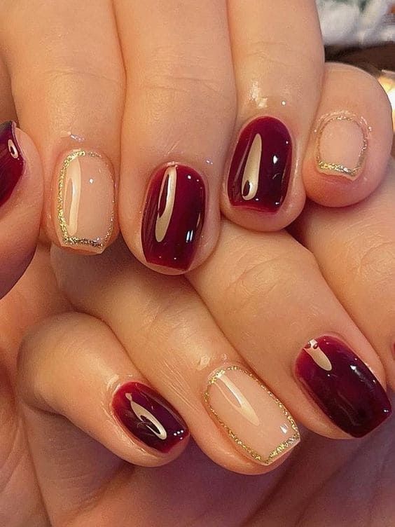 Elegant Deep Burgundy and Nude Nail Design with Glossy Finish and Gold Accents.