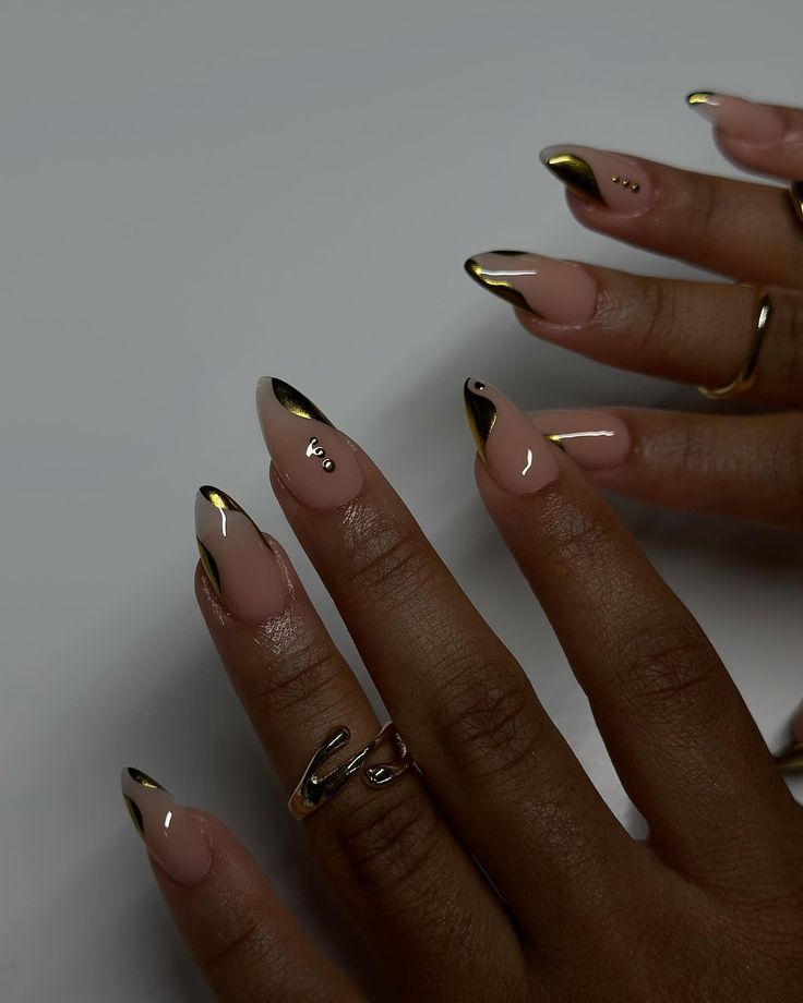 Chic Nude and Black Pointed Nail Design with Minimalist Embellishments and Gold Accents.