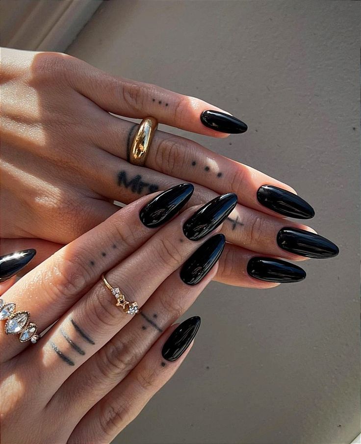 Chic Black Almond Nail Design Enhanced by Elegant Rings for a Bold, Confident Look.