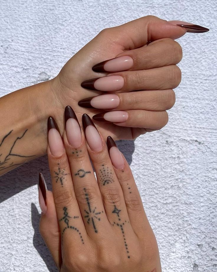 Chic Almond-Shaped Ombre Nail Design: Nude and Dark Brown Contrast With Intricate Tattoos.