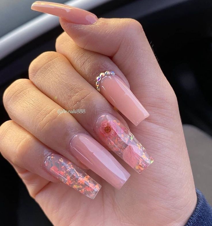 Sophisticated Nude and Translucent Nail Design with Floral Accents and Glamorous Rhinestone Embellishments.