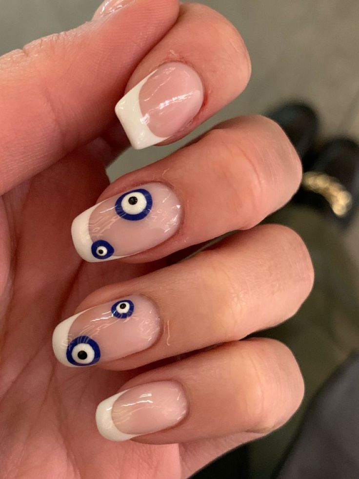 Chic French Manicure with Glossy Clear Polish and Playful Blue Evil Eye Accents.