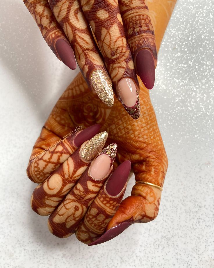 Sophisticated Almond-Shaped Nail Design: Matte Burgundy, Nude, and Glitter Accents with Henna Art.