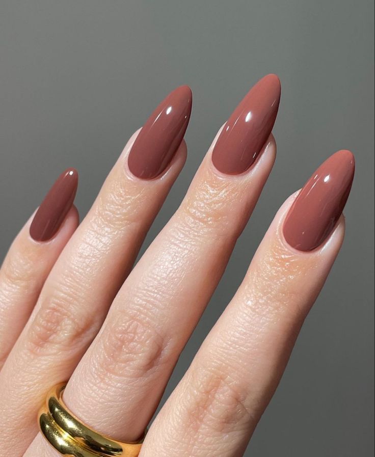 Sophisticated Almond-Shaped Nails in Glossy Warm Brown with Chic Elongated Tips and Gold Ring Accent.